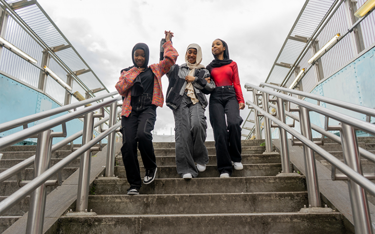 Three teen girls wearing hijabs holding hands descending concrete steps