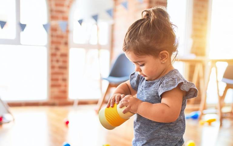 Toddler stood in a bright classroom holding a plastic cup