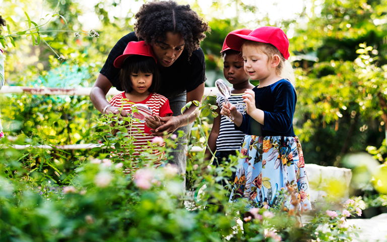 Woman showing young children plants outdoors under magnifying glasses. Credit: Rawpixel / Adobe Stock