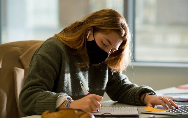 Young woman wearing a masking and writing in a notepad