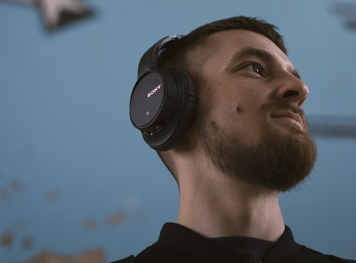 Man gazing up and away, wearing black headphones against a blue background