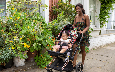 Young mother pushes baby stroller along a street full of plants. Credit: Cultura Creative