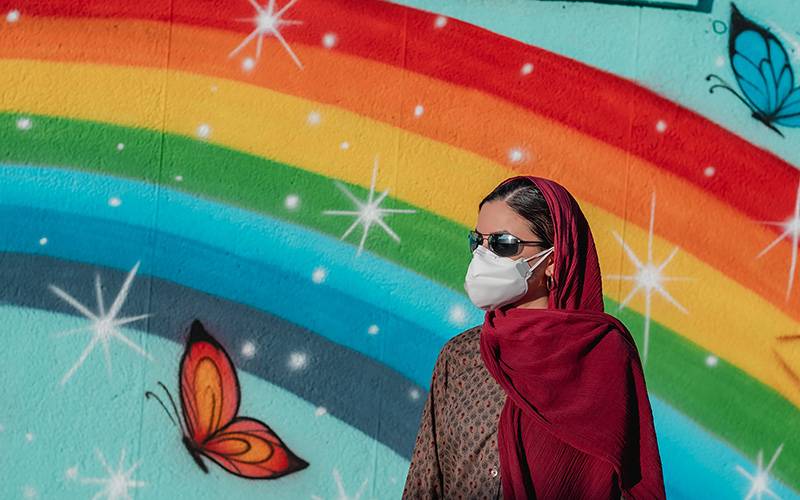 Woman standing in front of rainbow painting on wall. Image: Ashkan Forouzani via Unsplash