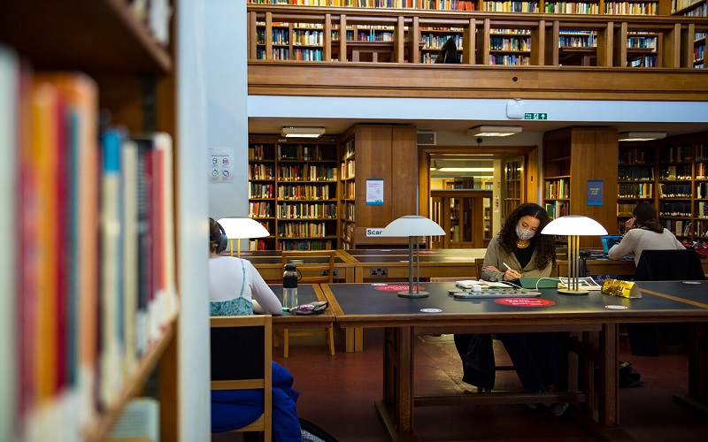 Students working in the UCL library with bookshelves in shot