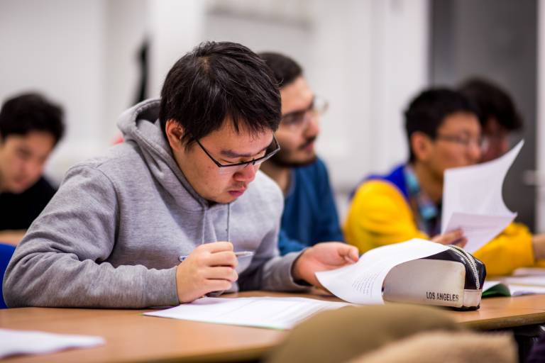 a UCL International Foundation (UPC) student in a grey jumper making notes in class 