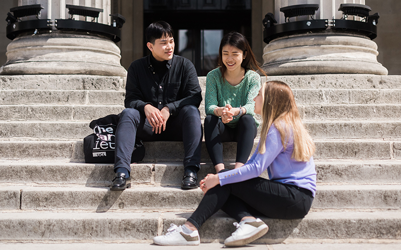 Three students sitting on stone steps in the university quad