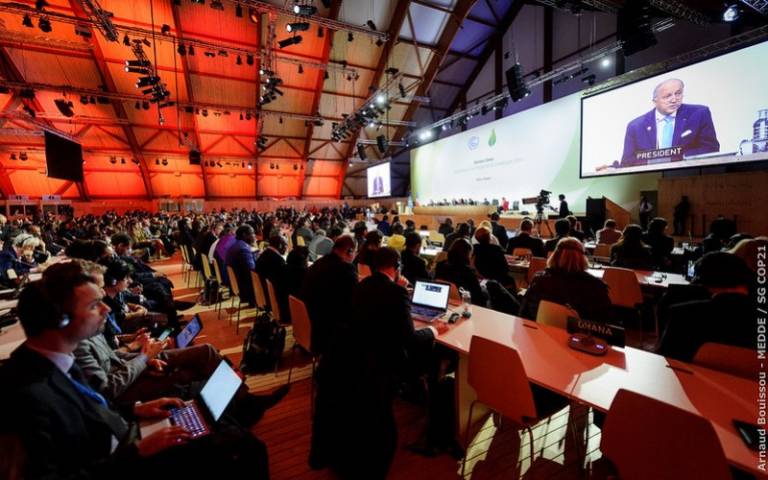 A large room with people sitting in rows looking at a screen at COP21 in Paris