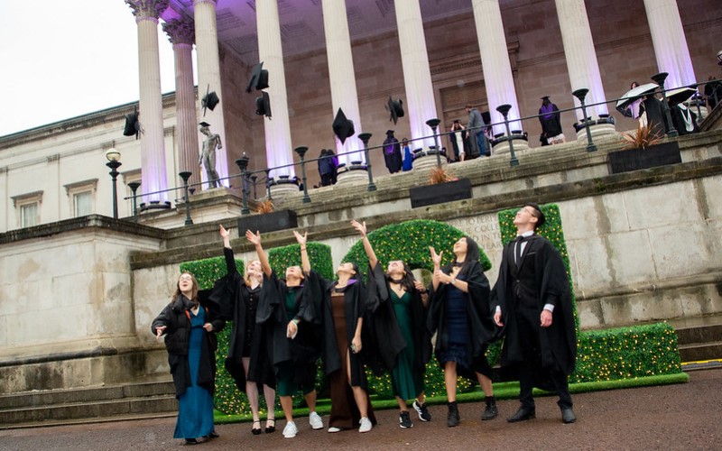 A group of people Laws graduates throwing their caps in the air at the March 2022 Laws Graduation reception