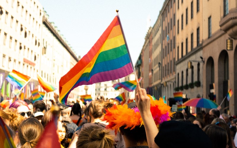 A person waving an LGBTQ+ flag in a crowd