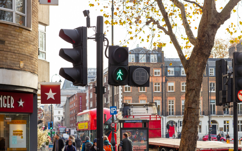 A green pedestrian crossing light at a street in London. In the background, there are buses, people walking and a cafe. 