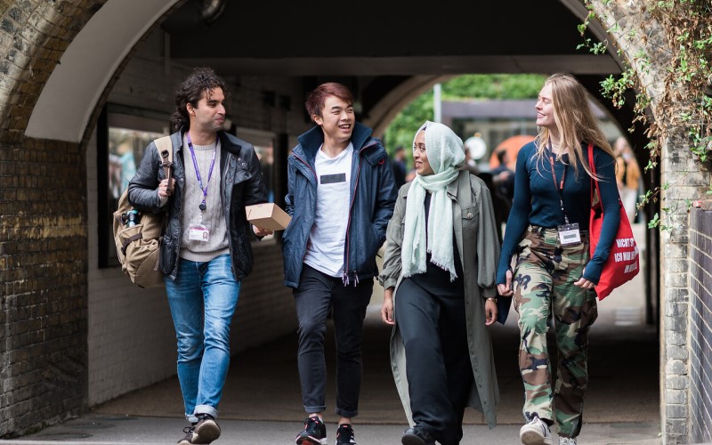 Four students walking along the south quad on the UCL campus, chatting and smiling