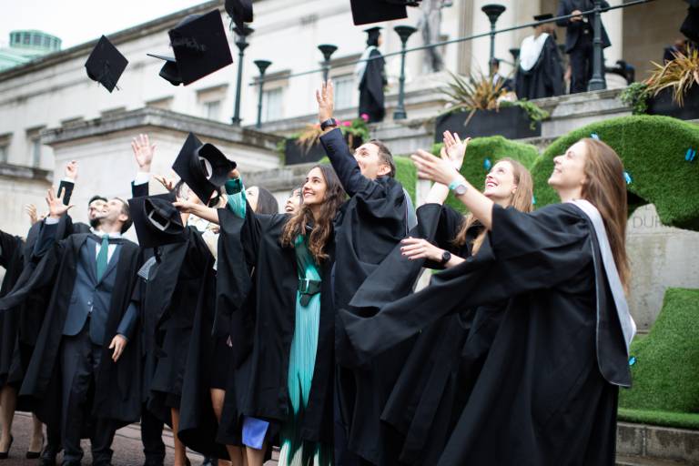 A group of UCL Laws graduates throwing their graduation caps in the air and posing for a photo