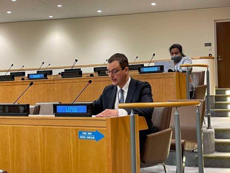 Dr Martins Paparinskis delivering a statement at the UN General Assembly’s Sixth Committee. Dr Paparinskis is sitting and speaking into a microphone behind a sign reading "LATVIA". Sitting in the row behind him is a woman with a sign reading "MADAGASCAR"