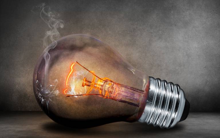 A lit lightbulb lying on its side with a hole in the side and smoke coming out.