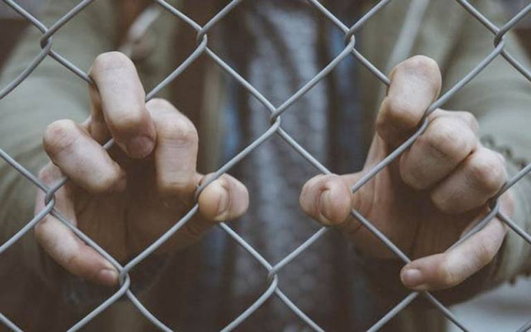 IMAGE: hands clutching at chain fence