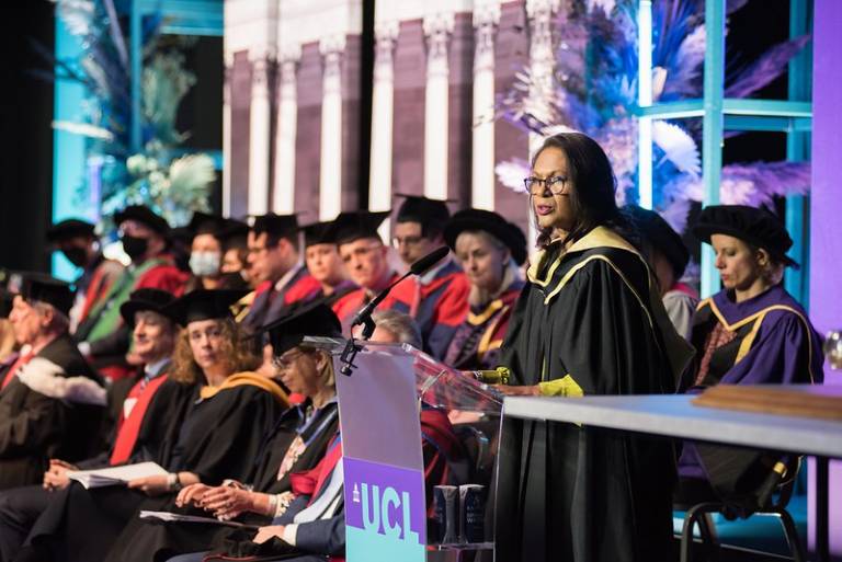 Gina Miller delivering her speech at the UCL Laws 2022 graduation ceremony. Behind her, various UCL Laws staff are sitting on the stage