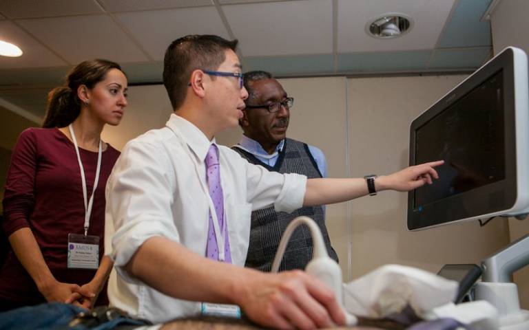 A person carrying out an ultrasound and pointing to a screen as two people look on. This photo was taken part of the Clinical Ultrasound in Hepatology: Training for Hepatologists