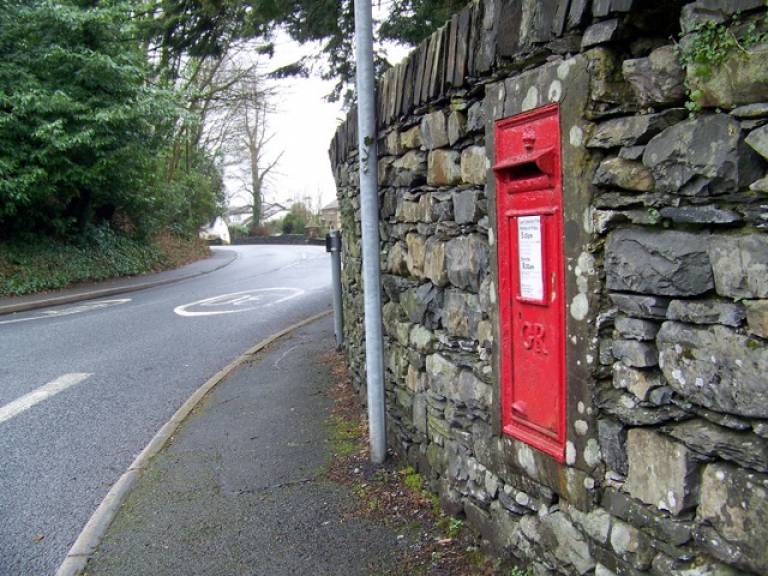 A red postbox in a brick wall on the side of a road