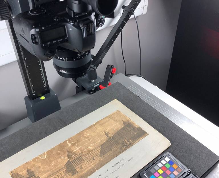 A camera lense sits in a stand above an old document showing an image of UCL.