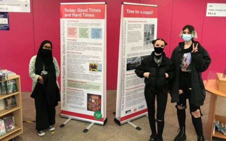 Three participants stand in front of The New Curators’ exhibition in East Ham Library.