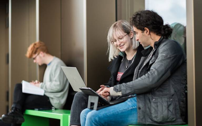 Library users sitting outside a building looking at laptop and tablet.