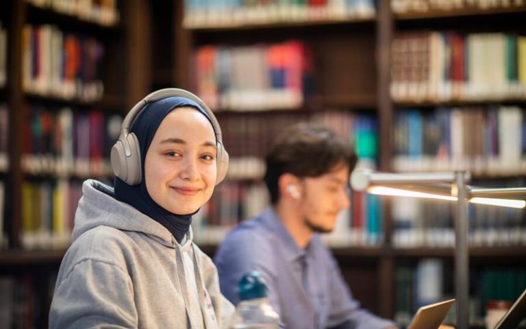 Student wearing headphones in the library and smiling towards the camera
