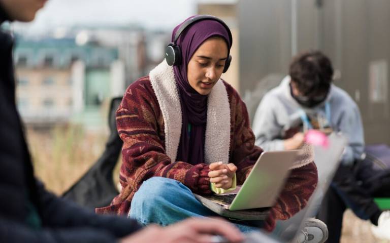 Students on campus. Focus on student wearing headphones and using a laptop.