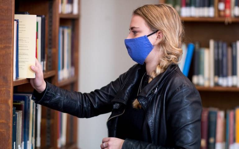 User taking an item from library shelf. User is wearing a protective mask.