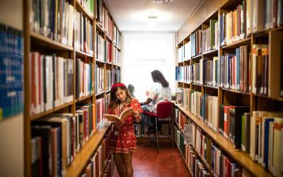 Student standing amongst book shelves, reading, inside the Main Library
