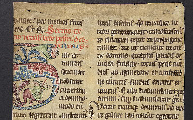 A section of medieval manuscript page with black script. On the right is a decorated S in blue and pink ink. The top of the S has a face in a green hood. The bottom of the S has a monster with the torso of a woman playing a fiddle.