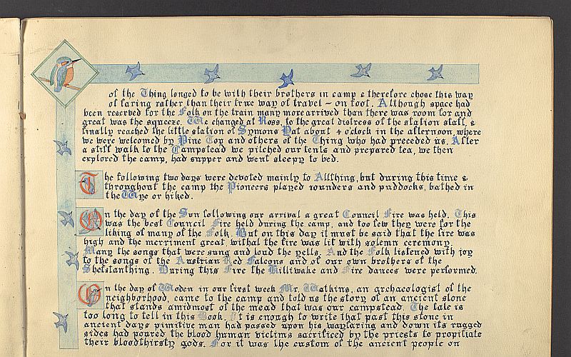 A page of written gothic-style text. Capital letters in blue. Letters at the beginning of paragraphs are red in blue squares decorated with kingfishers. Blue border decorated with kingfishers on top and left of page. Large kingfisher in left corner.