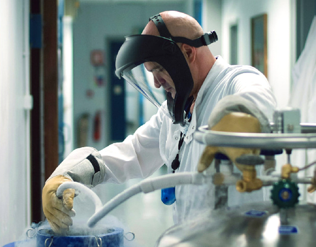 Scientist wearing face protection topping up liquid nitrogen to cryobank