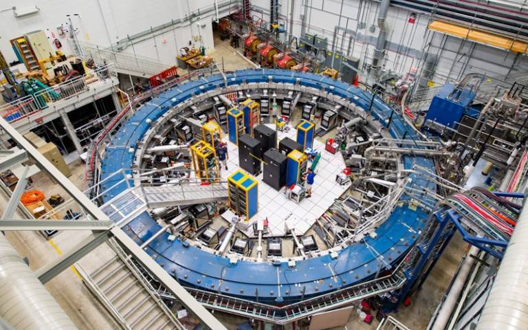     The Muon g-2 ring sits in its detector hall amidst electronics racks, the muon beamline, and other equipment. The experiment operates at negative 450 degrees Fahrenheit and studies the precession (or wobble) of muons as they travel through the magneti