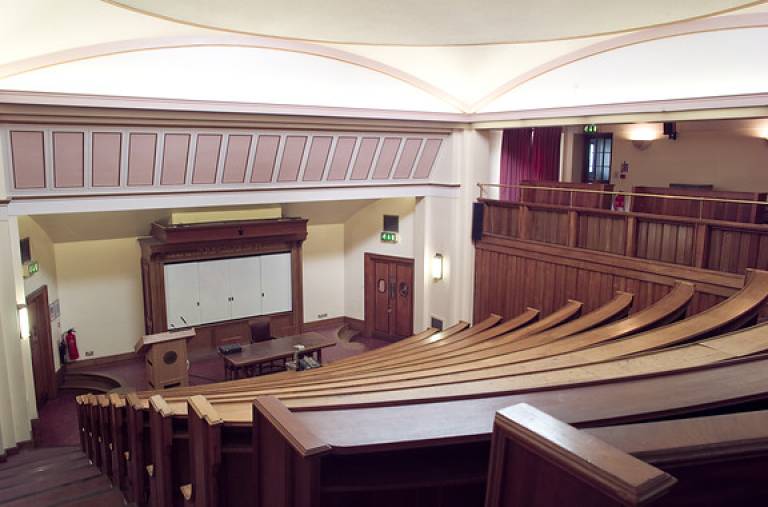A photograph of the Gustave Tuck Lecture Theatre, where the symposium was held. It is a raked, lecture theatre with historic wooden accents and a curved layout.