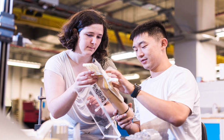 Two people in a lab working together on manipulating a robotic hand