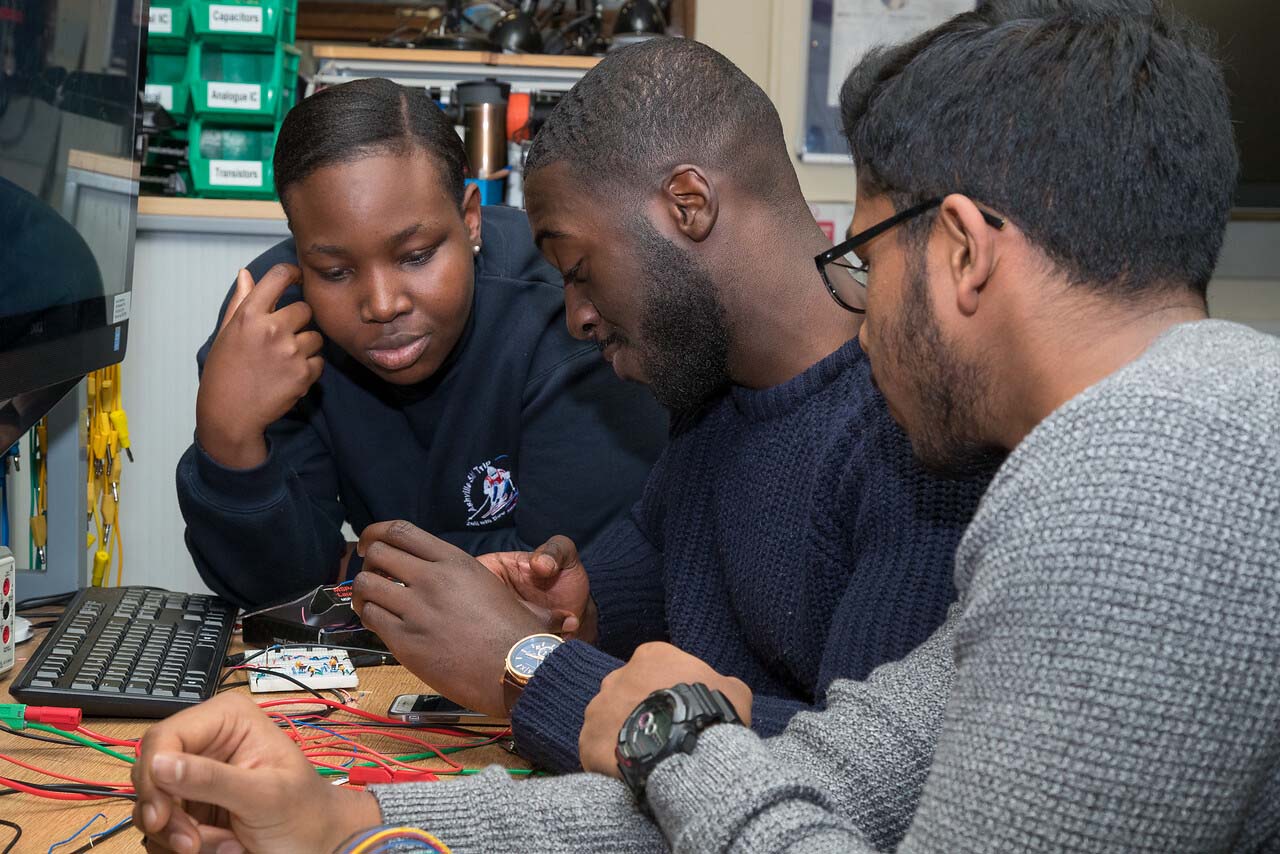 Three students working together over wires and circuitry