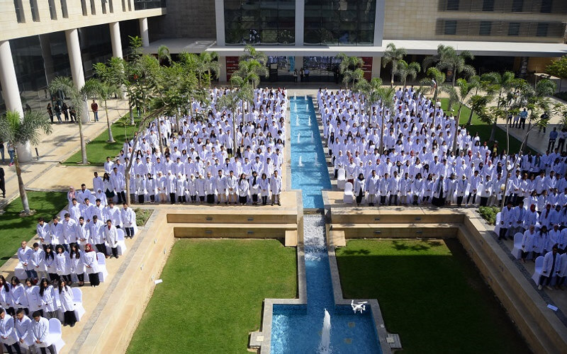 Graduating students in white medical coats assemble around the quad and water feature at NGU, Egypt