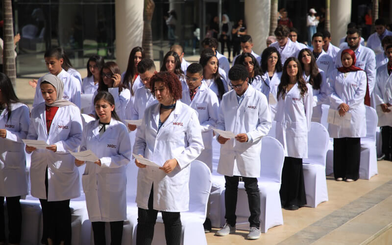 Graduating students in white medical coats stand during a ceremony at NGU, Egypt