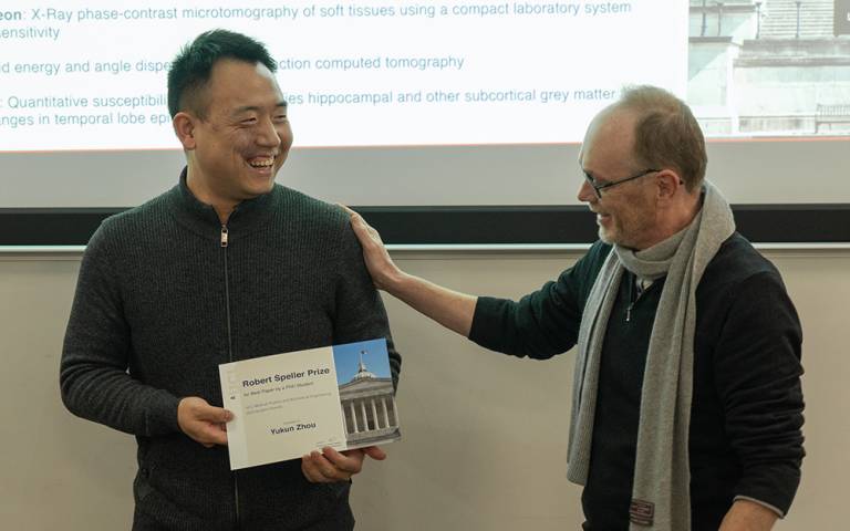 a student holding a certificate and an academic greeting him 
