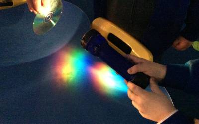 A photo of a child’s hand holding a torch and shining it on a compact disc to create a rainbow