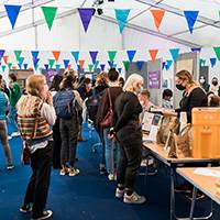 a picture from the UCL Welcome Week 2021 which shows students standing in a marquee lining up to chat to people at tables to join clubs