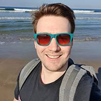 Picture of nick with sunglasses on standing on the beach with the sea in the background