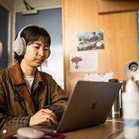 Female student sitting at her laptop with headphones on in her university halls room