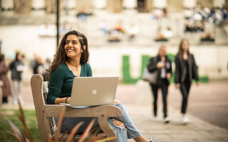 Student smiling with a laptop at UCL campus