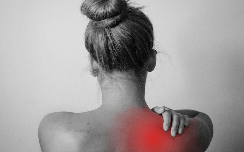 The back of a woman in greyscale with a pain region in the shoulder highlighted in red
