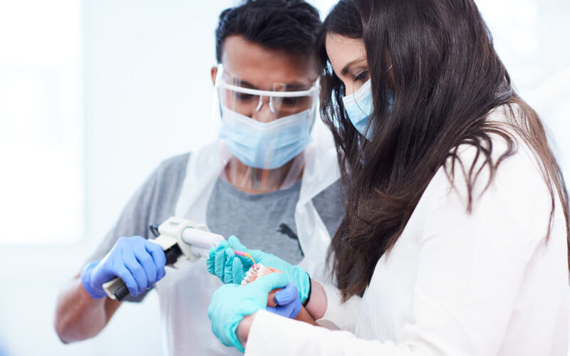 Two people in protective equipment practise using surgical equipment in the Eastman Dental Institute