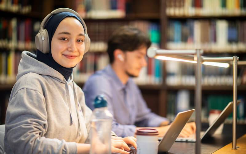 Two students in the UCL library, one smiling at the photographer