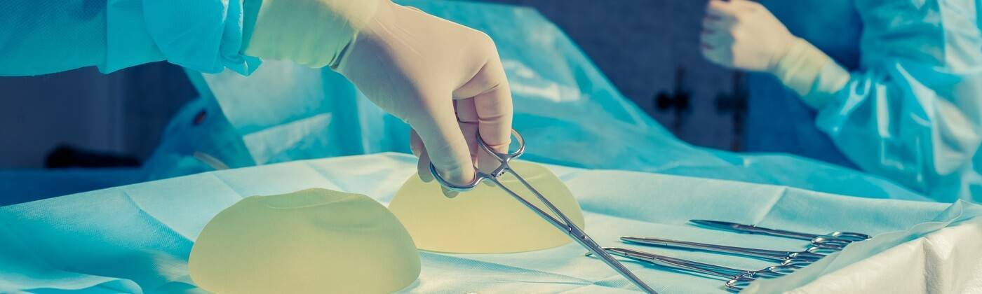 Surgeon reaching for surgical scissors on a table with silicon implants