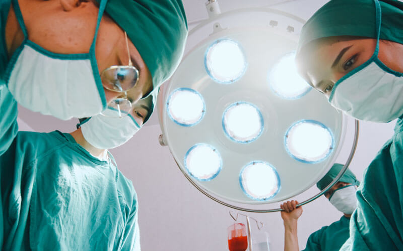 Surgeons working on a patient, with one holding the surgical light