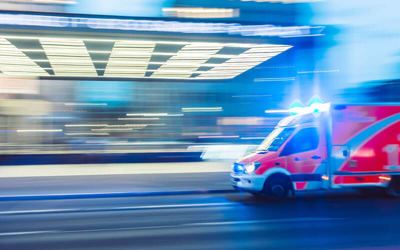 Ambulance travelling past a lit building at speed